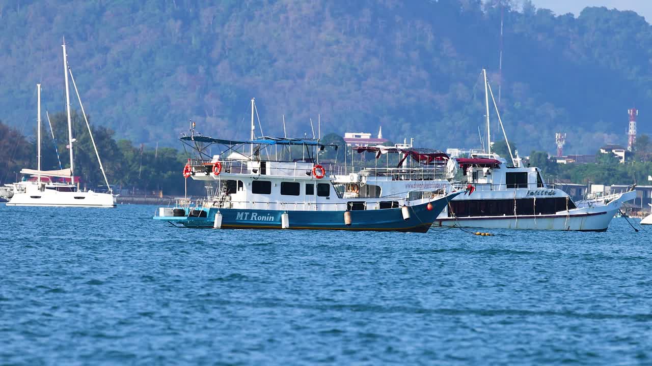 A fishing boat moves steadily across the blue ocean near Phuket, Thailand, under clear skies with distant hills in the background