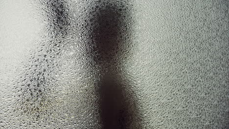 a female silhouette behind the frosted glass moves slowly