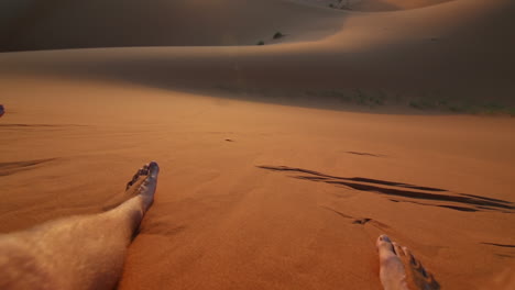 tilt up shot towards the sunset with a backpacker hanging his feet in the dunes