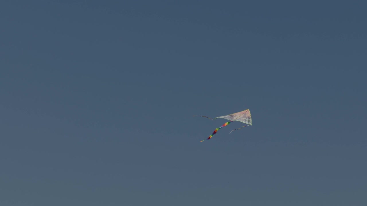 Un aquilone classico con una coda colorata che si libra nel vento in un cielo blu limpido e senza nuvole. Scatto naturalistico all'aperto in stile minimalista a tema libertà e divertimento.