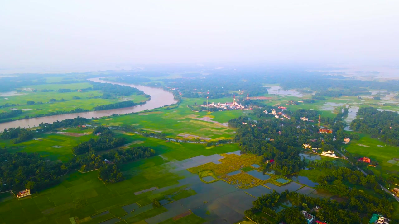 Luftfoto af landlige Bangladesh med en bugtende flod og smogfyldt himmel.