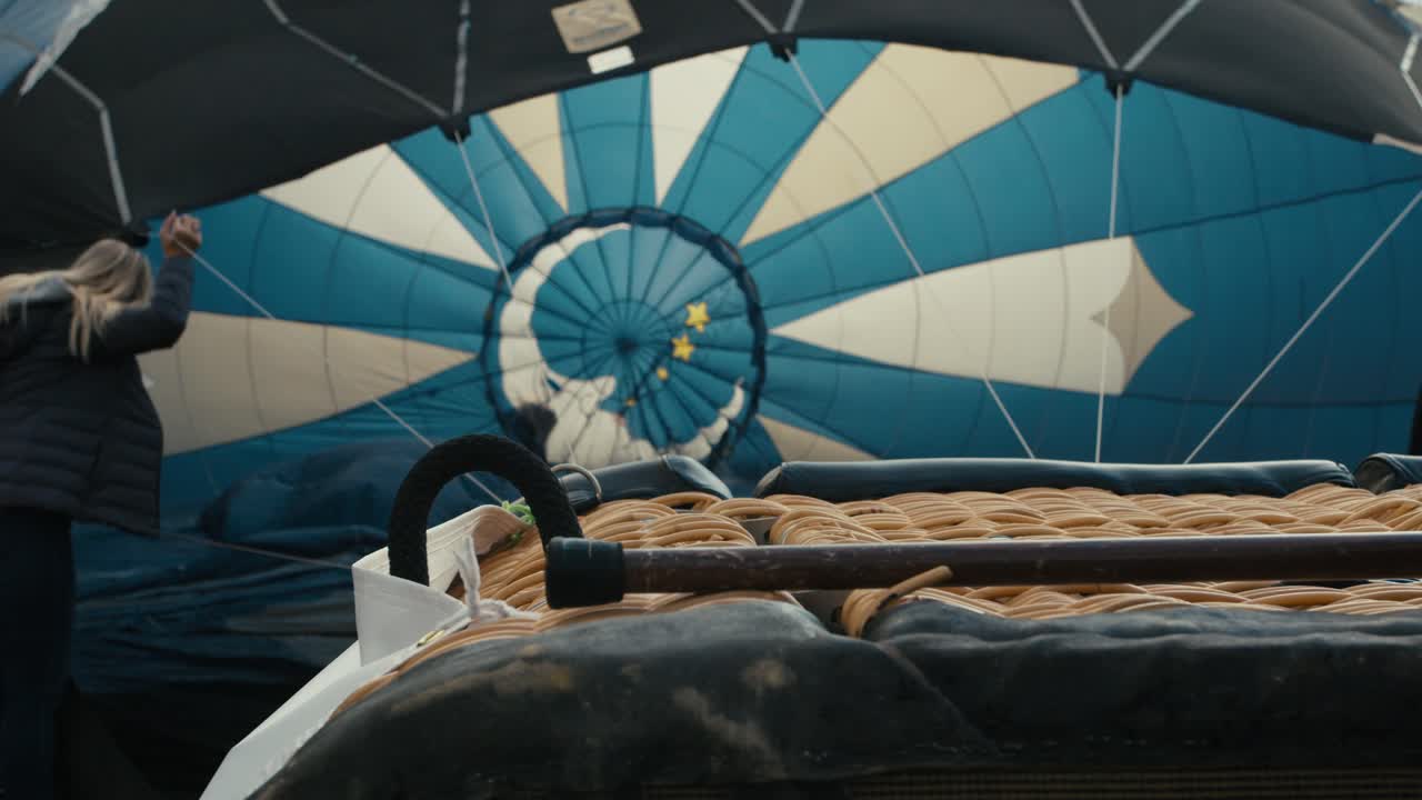 추운 겨울 아침 해가 뜨면 팬이 풍선을 바닥에 부풀리는 동안 열기구 바구니에서 열기구 내부로 초점을 맞춥니다.