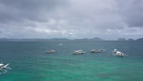 Drone-flying-above-small-fishing-boats-on-turquoise-water-and-natural-archipelago-paradise-in-El-Nido,-Palawan,-Philippines