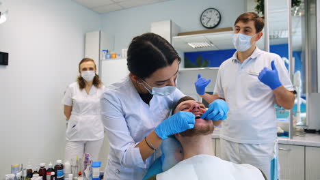 female student trying on the wire on the bracket system of a patient. male teacher is talking at backdrop.