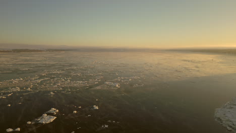 Vista-De-Drones-Hacia-Atrás-Yendo-Hacia-La-Costa-De-La-Ciudad-Canadiense-De-Beaumont,-Quebec,-Desde-La-Vía-Marítima-Del-Río-San-Lorenzo,-En-Una-Mañana-De-Invierno-Muy-Fría