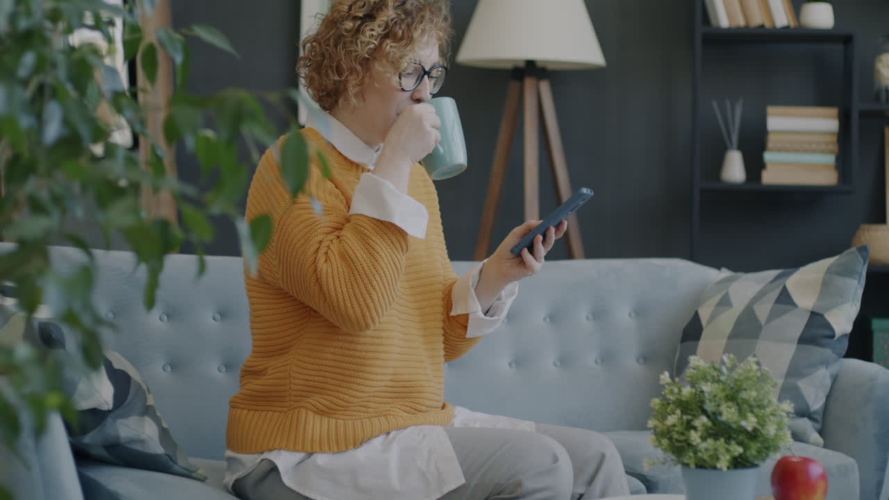 Woman relaxing on a couch, drinking coffee and using her phone