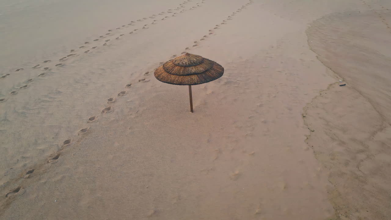 Lonely straw umbrella empty beach aerial view. Beige sandy surface footprints