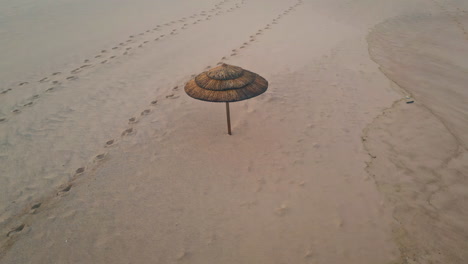 sombrilla de paja solitaria playa vacía vista aérea. huellas de superficie de arena beige