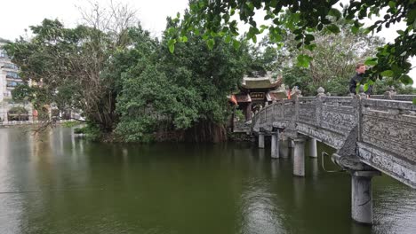 people walking across a temple bridge over a lake