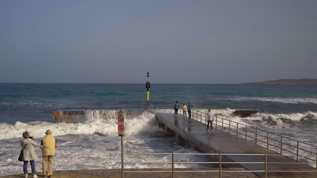 olas del océano rompiendo en un par de piedra en mallorca con grandes salpicaduras y gente en el par