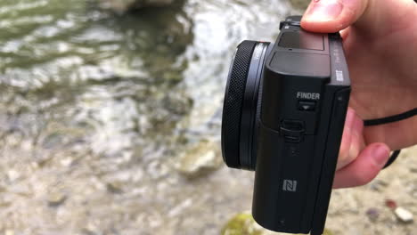 side view of a compact camera next to a river, outdoor filmmaking, technology