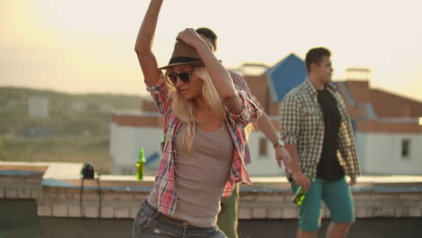 una joven mueve hermosamente sus brazos y cuerpo en un baile en el techo. su cabello y camisa se están desarrollando en el viento. está bailando y disfrutando con sus amigas en la fiesta.