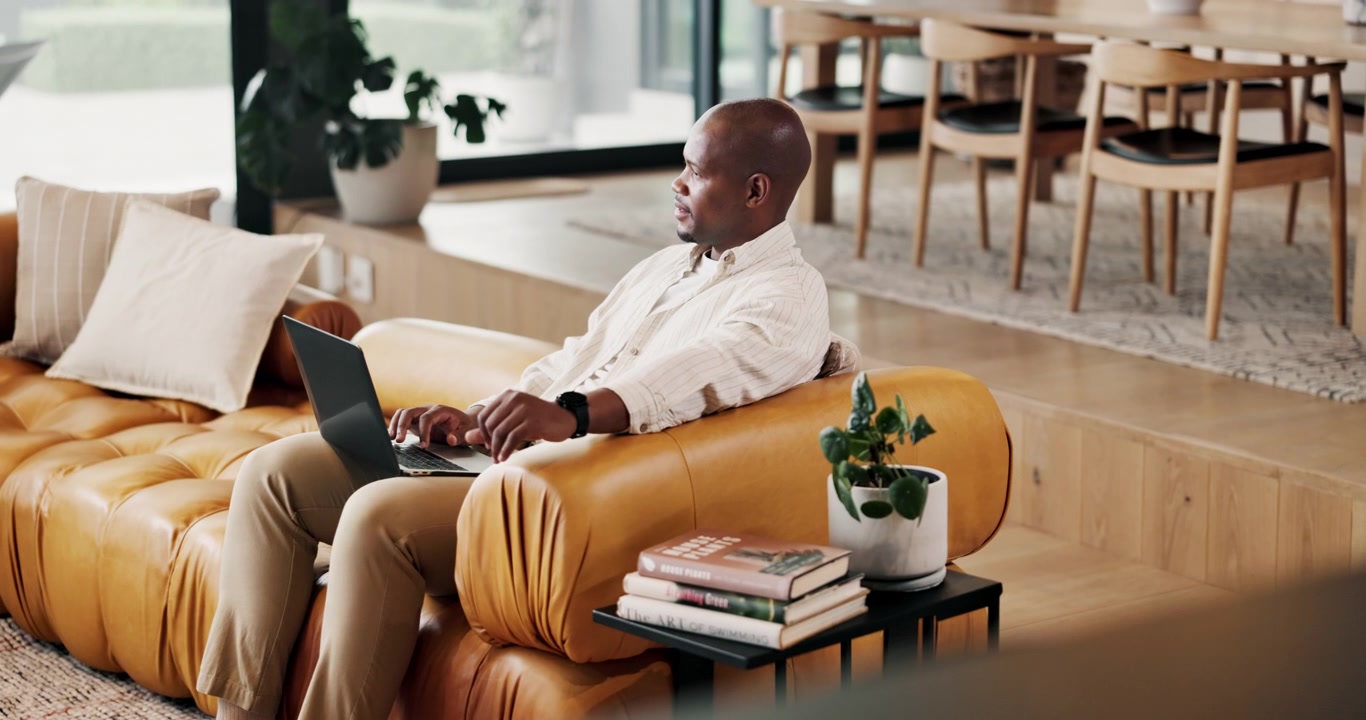 Man Working on Laptop While Sitting on Leather Sofa at Home