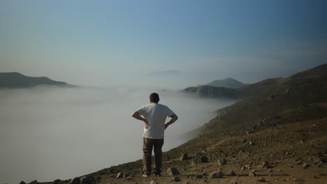 un hombre de pie en la cima de una cordillera por encima de las nubes, mirando hacia el horizonte