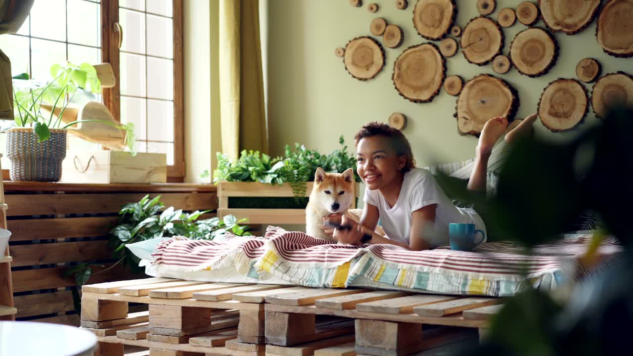 una niña alegre está viendo la televisión con su lindo cachorro sosteniendo el control remoto, presionando botones y riendo mientras el animal disfruta del amor y el cuidado.
