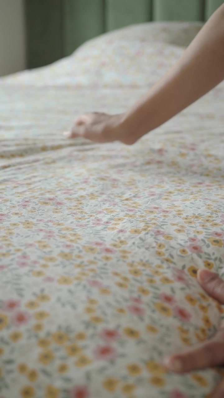 Seseorang merapikan seprai bermotif bunga di kamar tidur.