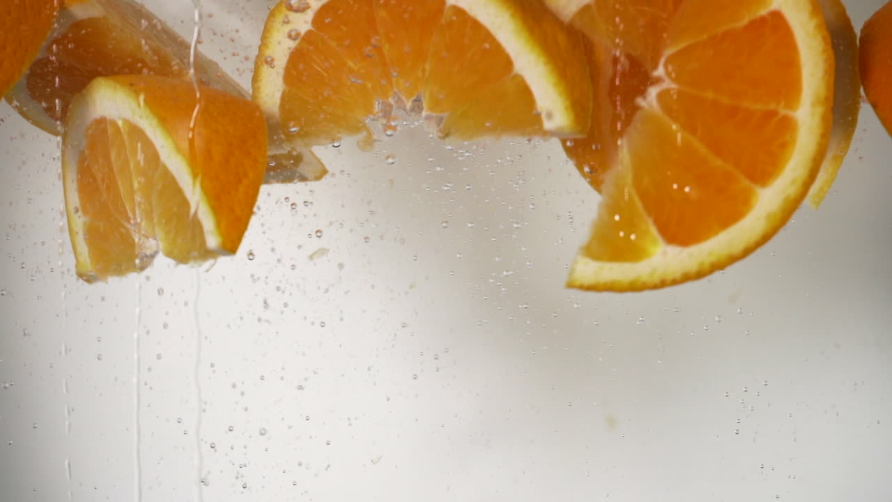 rallentatore cunei arancioni che cadono in acqua, rinfrescanti arancioni che cadono in fondo bianco dell'acqua