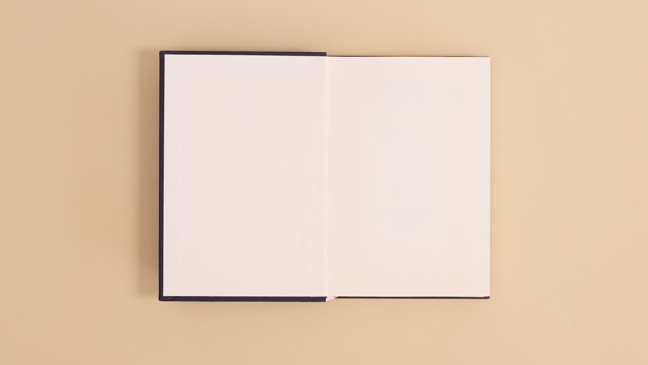 Dark blue hardcover vintage book appear and open with copy space on beige background. Stop motion flat lay