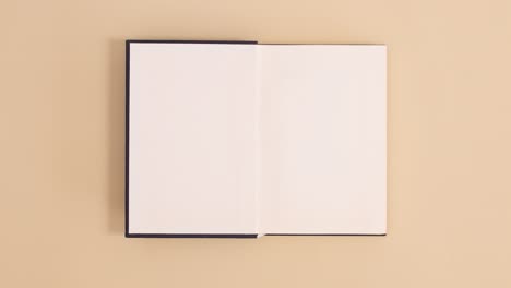 dark blue hardcover vintage book appear and open with copy space on beige background. stop motion flat lay