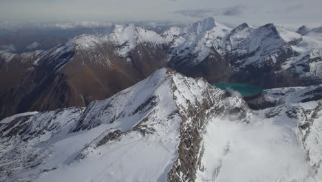 Drone-shot-of-green-mountain-lake-surrounded-by-snowy-alps-in-Austria