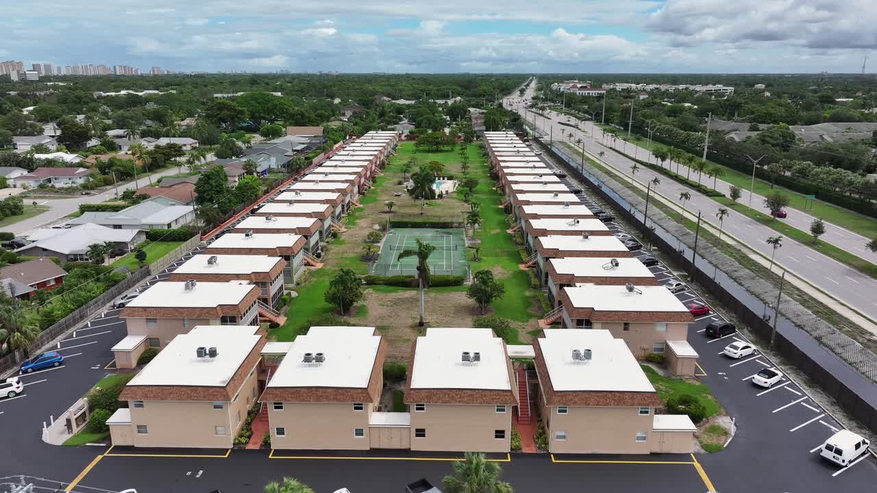 Aerial flyover Apartment houses with private tennis field in Suburb of Naples City beside highway. Florida, USA.
