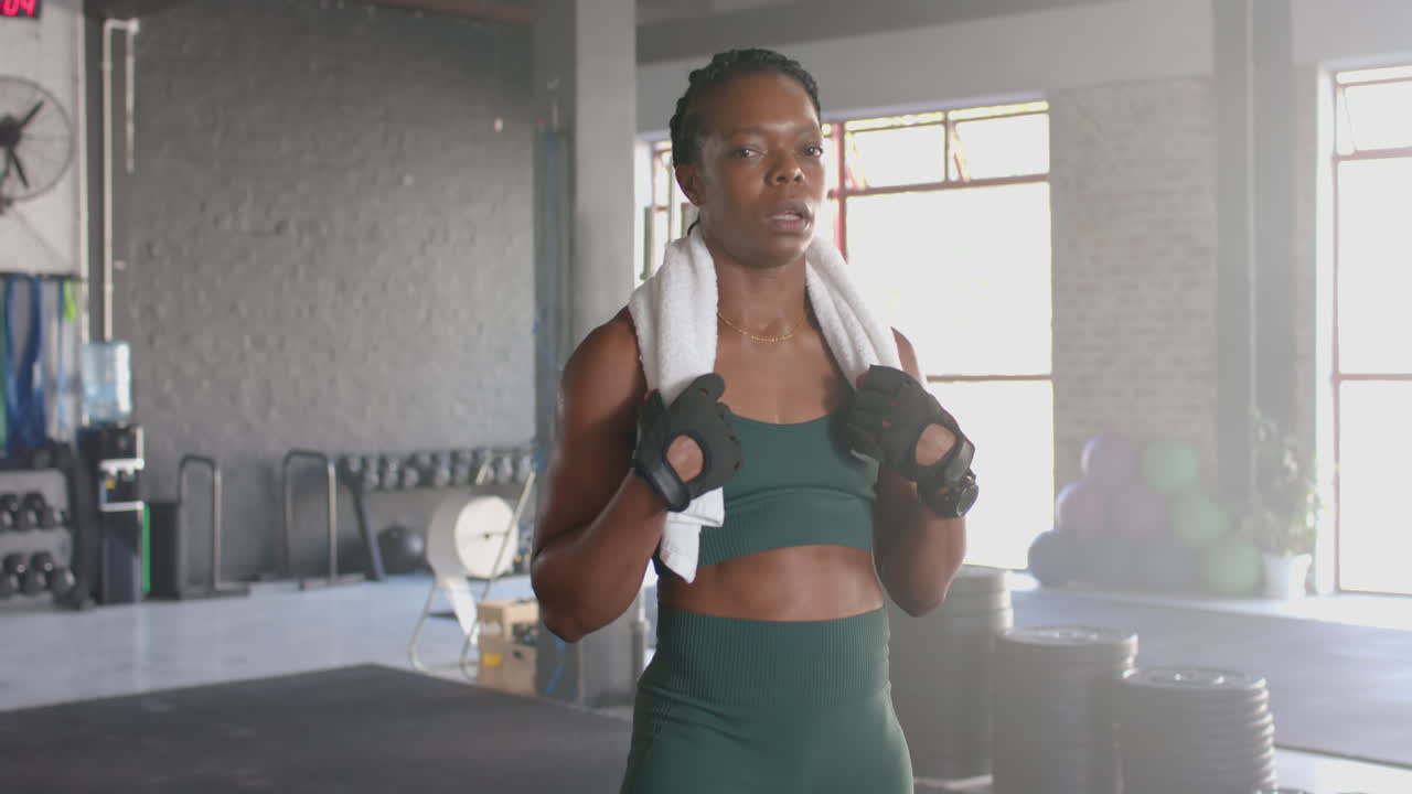 Holding towel and wearing workout gloves, woman taking break in gym