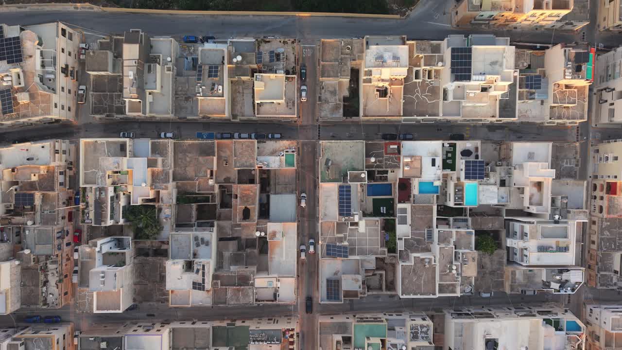 Vista aerea dall'alto di una città maltese che mostra una griglia di strade strette e tetti densamente affollati. I tetti piatti, i pannelli solari e le terrazze panoramiche riflettono lo stile di vita mediterraneo