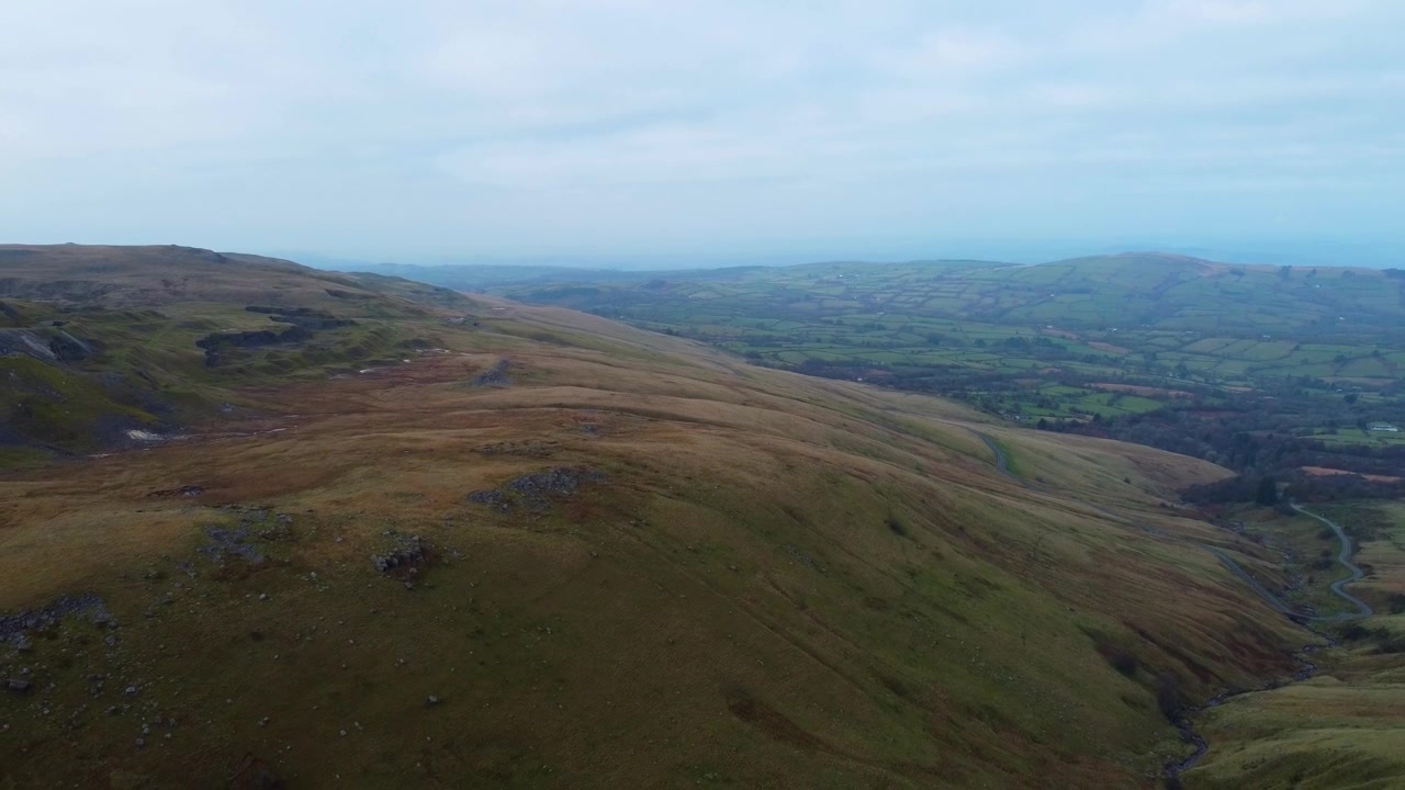 Bredt, tilbagetrækkende luftfoto af landbrugslandskab i Brecon Beacons Nationalpark, Wales. Landskab med blå dis i horisonten og gammelt kalkstensbrud 4K