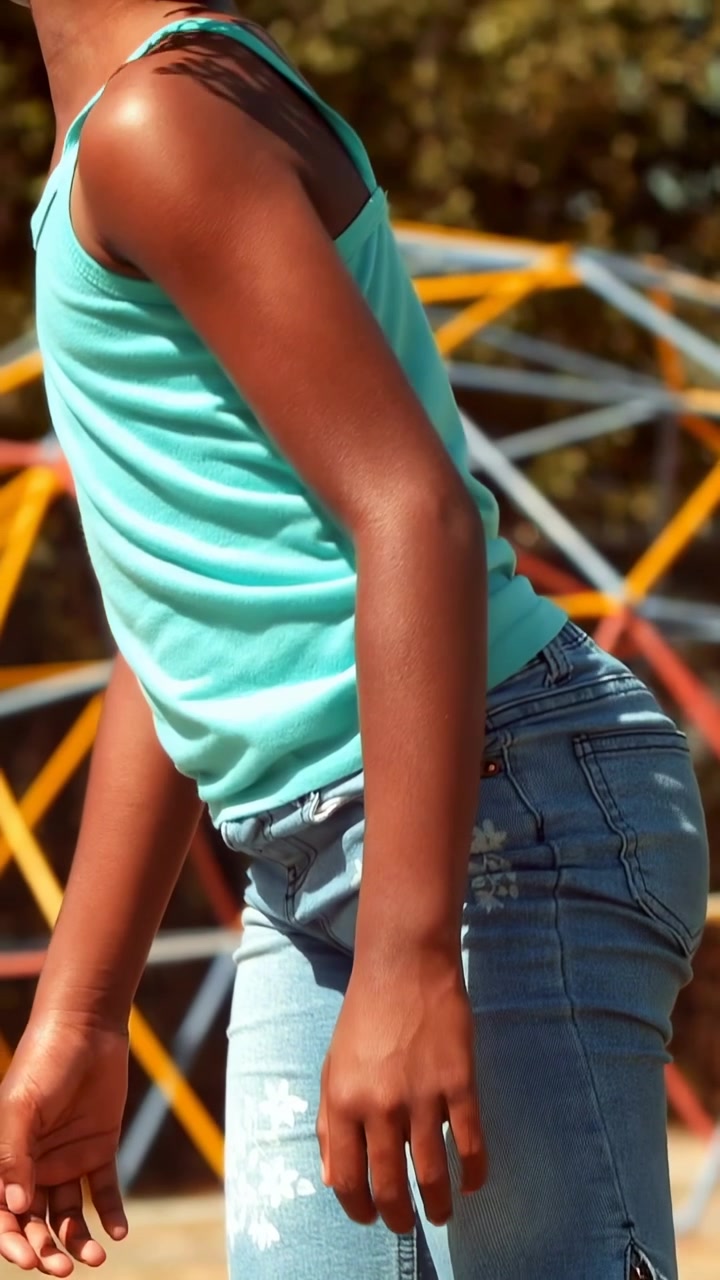 Vertical video: Shifting weight, girl stepping to cross low wooden beam at park, wearing teal tank