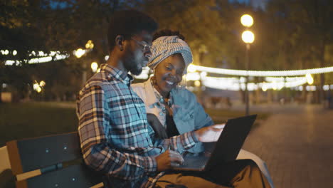 african american man and woman using laptop in park in evening