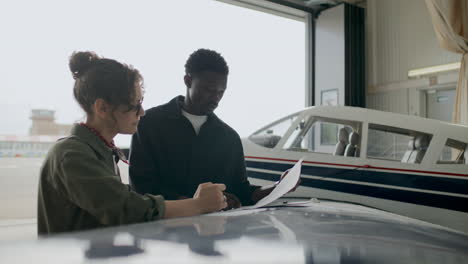 diverse aircraft mechanics discussing paper plans in hangar