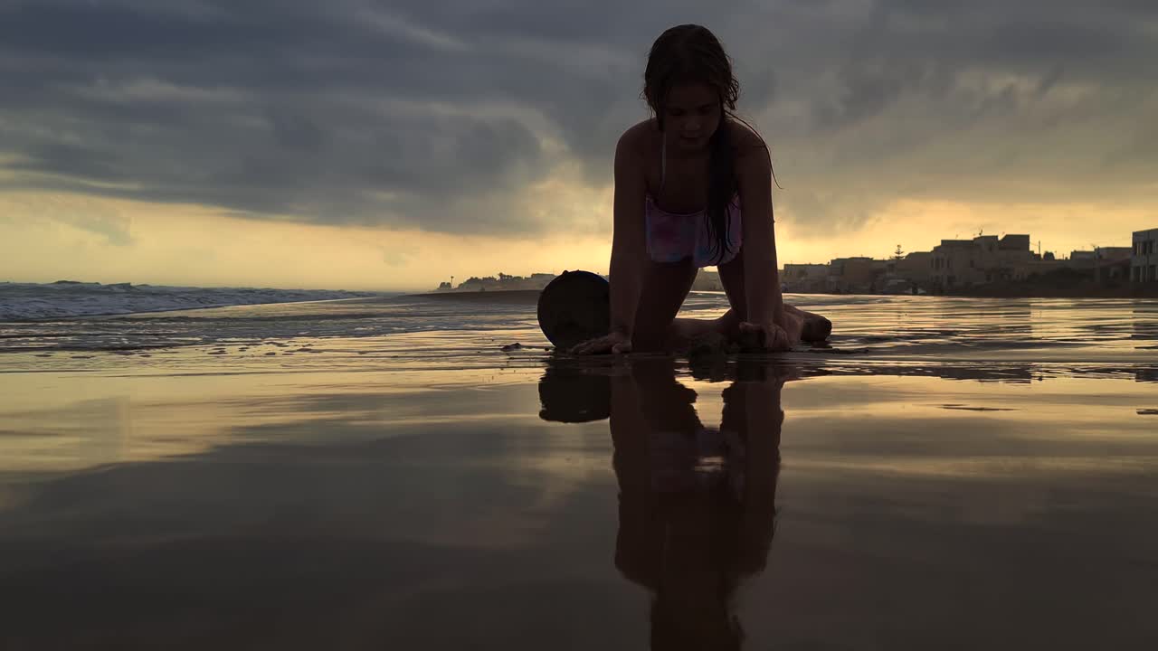 ángulo bajo único de hermosa niña caucásica jugando con balde y arena en la playa al atardecer