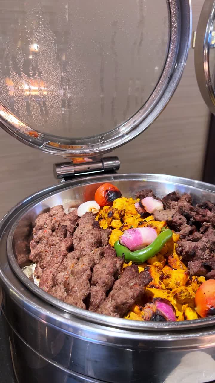Hot steam rises from a shiny buffet tray filled with grilled kebabs, juicy chicken tikka, and roasted veggies. Captured in crisp vertical 4K, ideal for food and hospitality content.