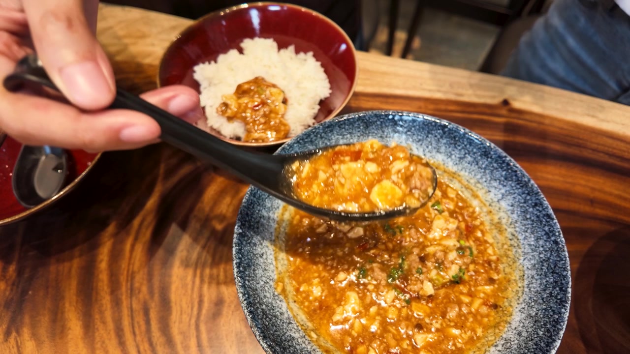 Bir kişinin baharatlı mapo tofu yemeğini siyah bir kaşıkla beyaz pirincin üzerine kepçeyle koymasının yakın çekimi.