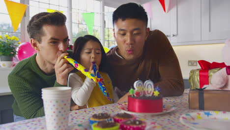 family with two dads and daughter celebrate parents 30th birthday at home with cake and party blower