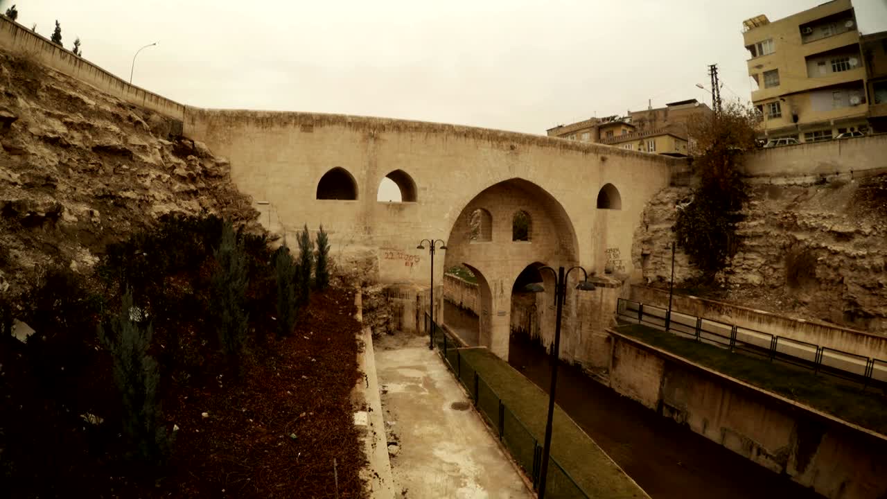 Motocicletta attraversa vecchio ponte sotto un antico canale a Sanliurfa, vista dal basso, giornata invernale nuvolosa