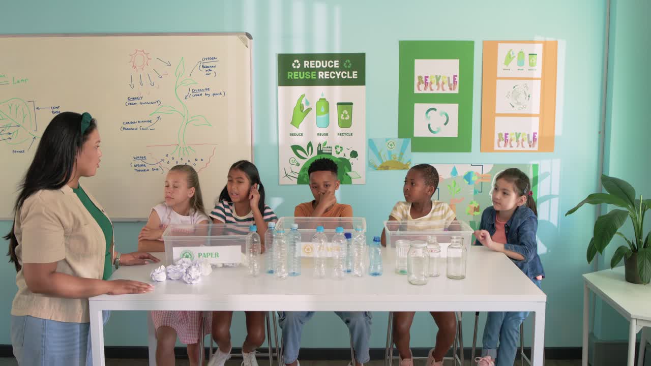 Teacher with five students asking about recycling at long white table, group sorting into PAPER bin