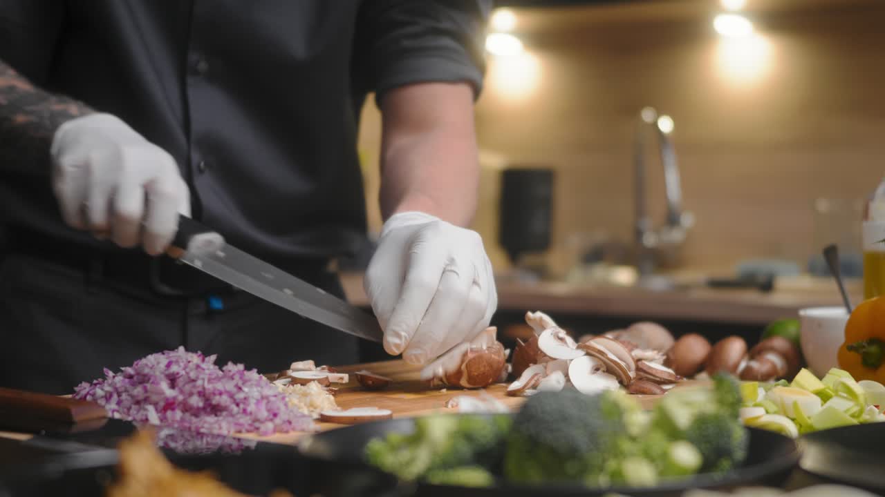champiñones cortados en una tabla de madera por un chef profesional con un elegante pantalones negro con tatuajes y guantes blancos
