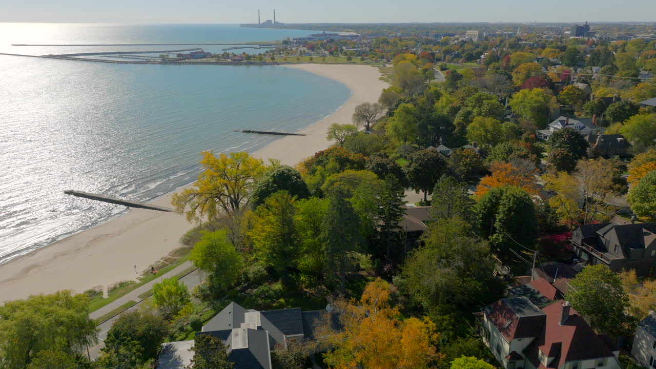 Drone aerial flyover of Sheboygan, Wisconsin neighborhood houses and autumn trees toward the Lake Michigan shoreline shimmering in bright sunlight on a beautiful day