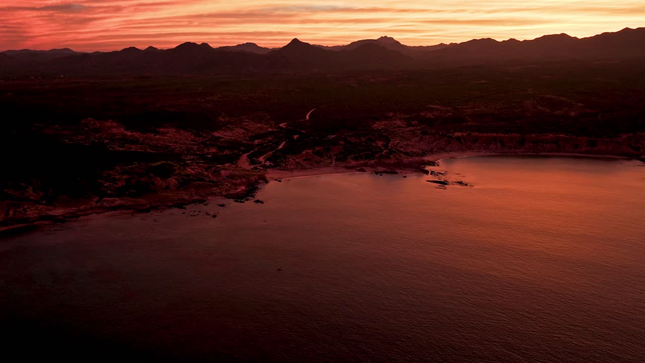 el avión no tripulado desciende sobre las nubes rojas naranjas del atardecer con la playa de cabo pulmo debajo