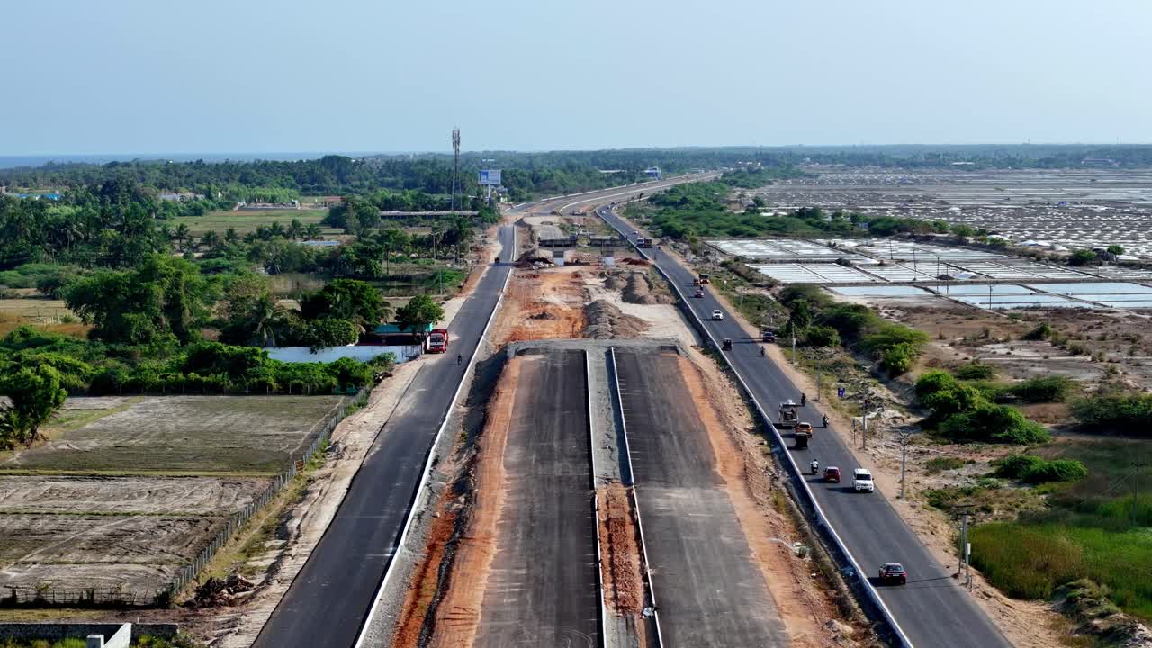 Aerial video of a highway under construction finished and unfinished sections. It dissects a landscape of lush green fields and vast salt pans, symbolizing the intersection of progress and nature