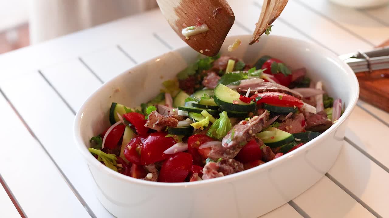 Hands mix vibrant beef salad with fresh vegetables in a bright kitchen. Natural lighting enhances the colorful ingredients