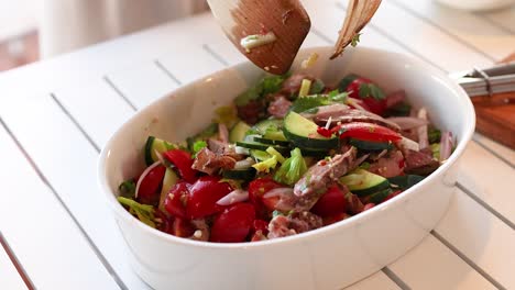 hands mix vibrant beef salad with fresh vegetables in a bright kitchen. natural lighting enhances the colorful ingredients