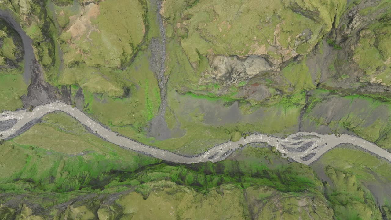 A striking aerial view of a braided river cutting through a lush green valley in Hafursey, Iceland, showcasing natural patterns and rugged terrain.