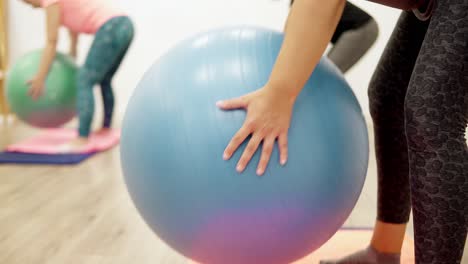 Mujeres-Jóvenes-Que-Realizan-Ejercicios-De-Doblado-Sobre-Filas-Para-La-Estabilidad-Del-Hombro-Y-El-Brazo-Usando-Una-Pelota-Suiza-De-Ejercicio-Físico-En-Una-Clínica-De-Fisioterapia-Deportiva,-Cerrar