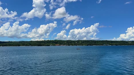 a lone fishing boat floats on tropical waters with island backdrop and dramatic cloud formations—great for travel or lifestyle use