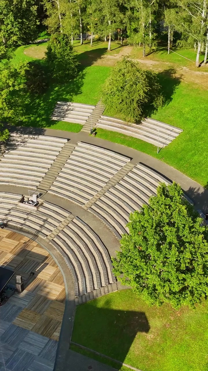 People Setting Up Stage For Concert Event At Sauleskalna Estrade In Talsi, Latvia. - aerial vertical shot