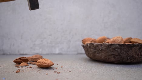 person opening hard shell of almond nuts with hammer