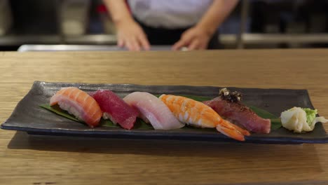 A sushi chef presents his beautifully plated fresh nigiri sushi with 5 different types and flavours with a side of pickled ginger