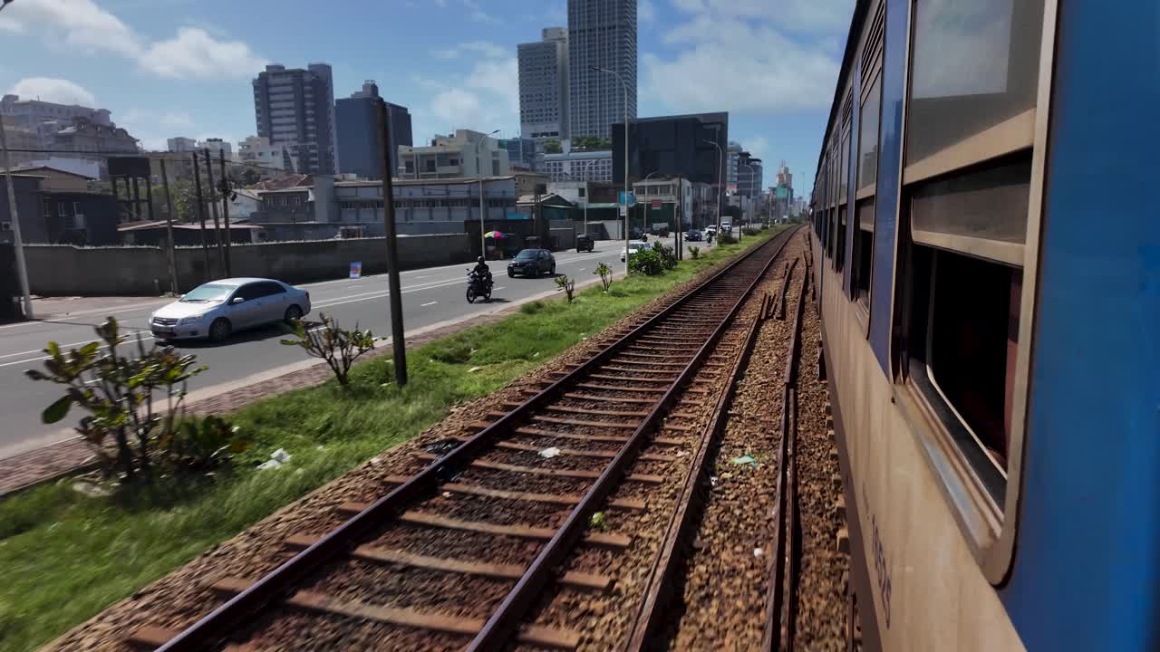 A view from a train traveling beside a bustling roadside in Colombo, Sri Lanka, illustrating urban life and transportation.